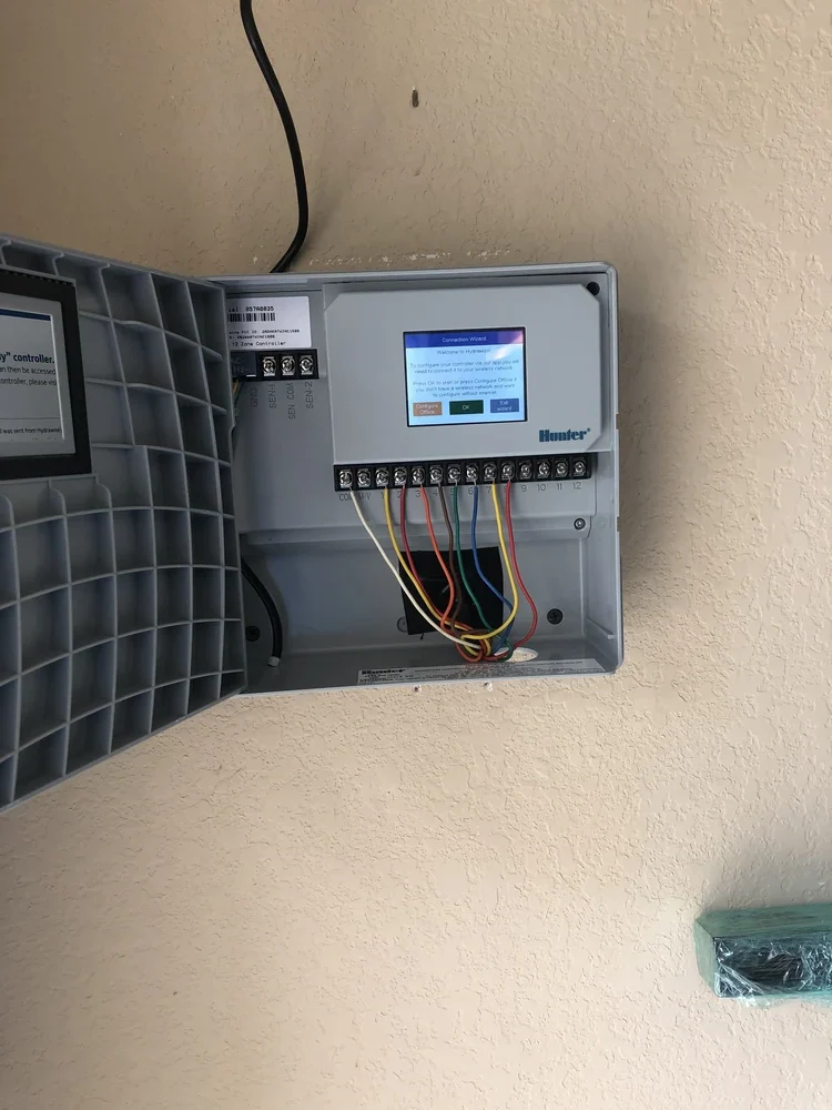Open Hunter irrigation controller with colored wires connected inside a wall mounted gray control box.
