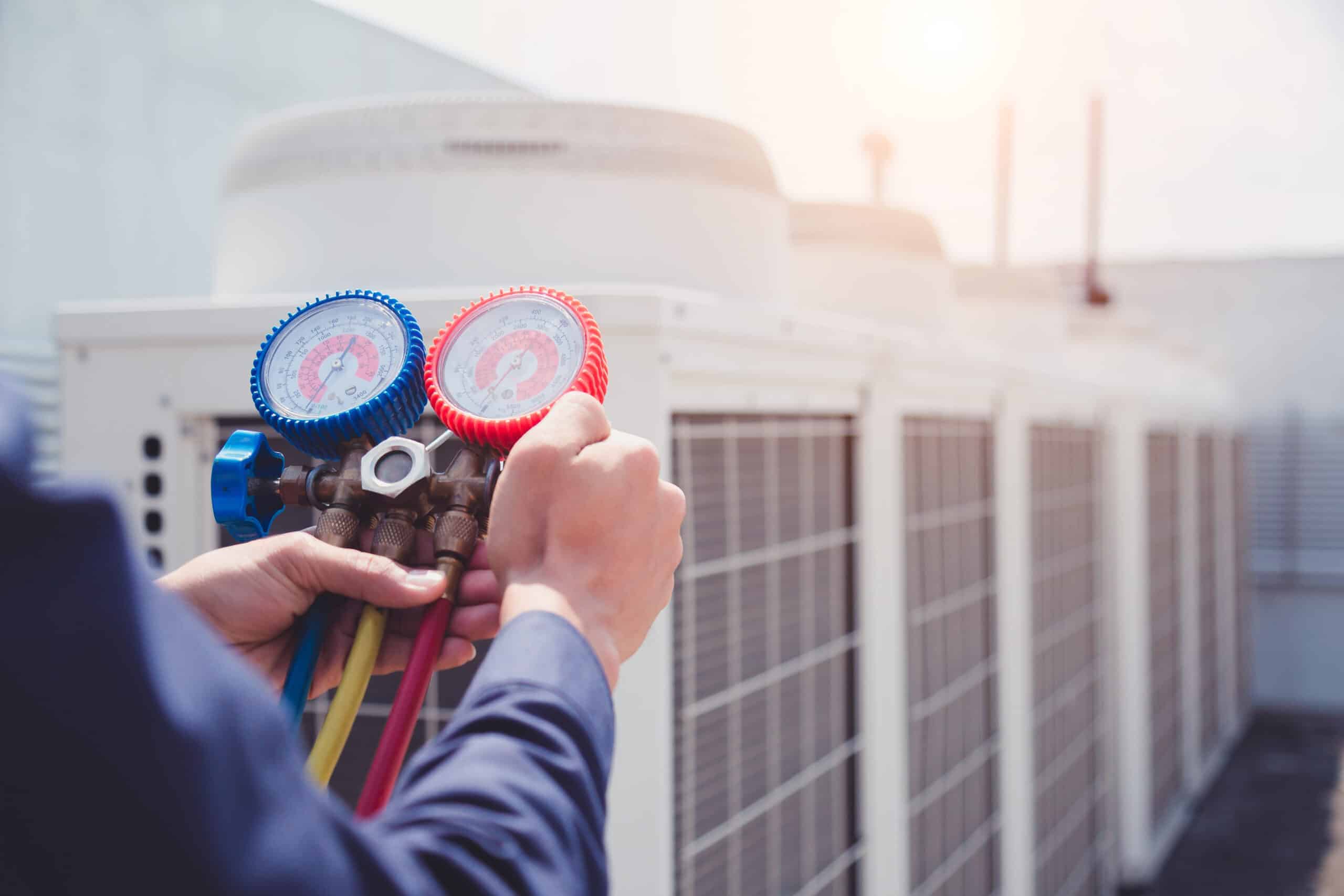 a professional conducting leak detection on an air conditioner unit by checking red and blue handheld meters