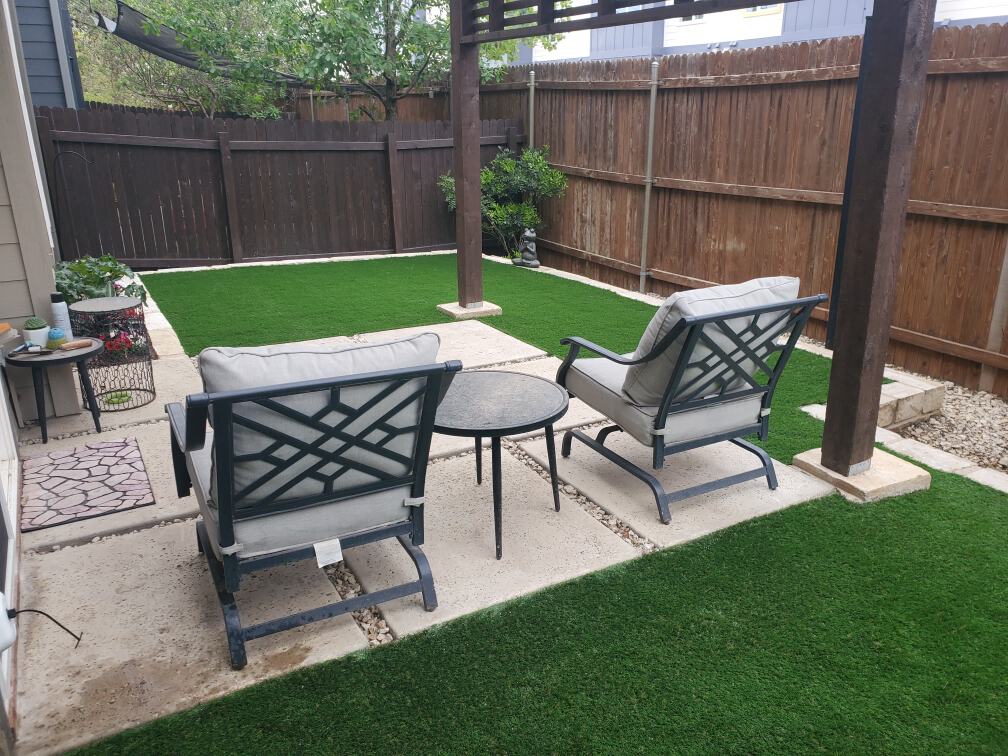 a small fenced-in backyard with a new landscape design featuring artificial turf, new plants, and outdoor furniture