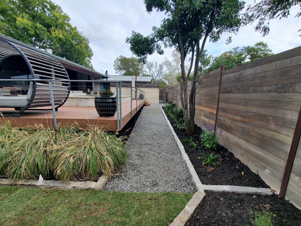 a fenced-in property with black mulch flowerbeds and native shrubs surrounding a custom deck