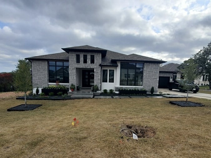 a large modern home with landscaping and two fledgling trees planted in a vast yard