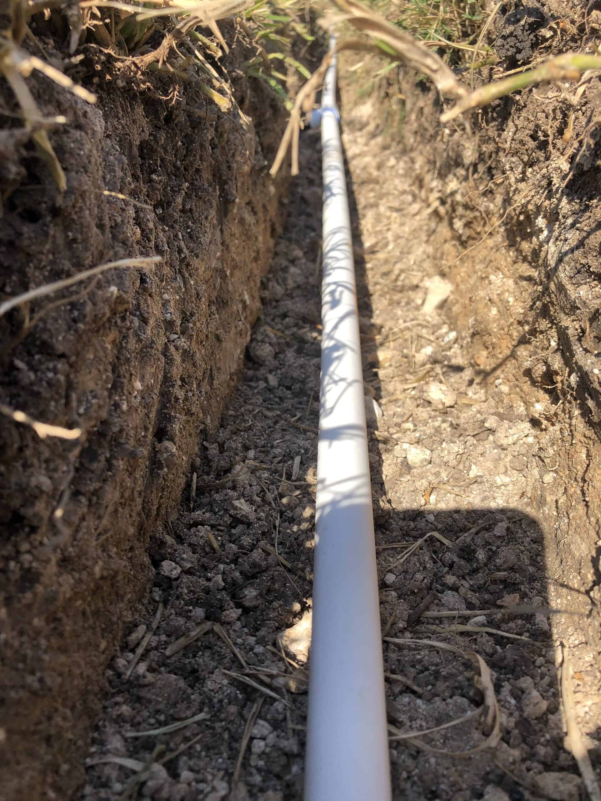 a long white irrigation pipe running along the ground in a small ditch