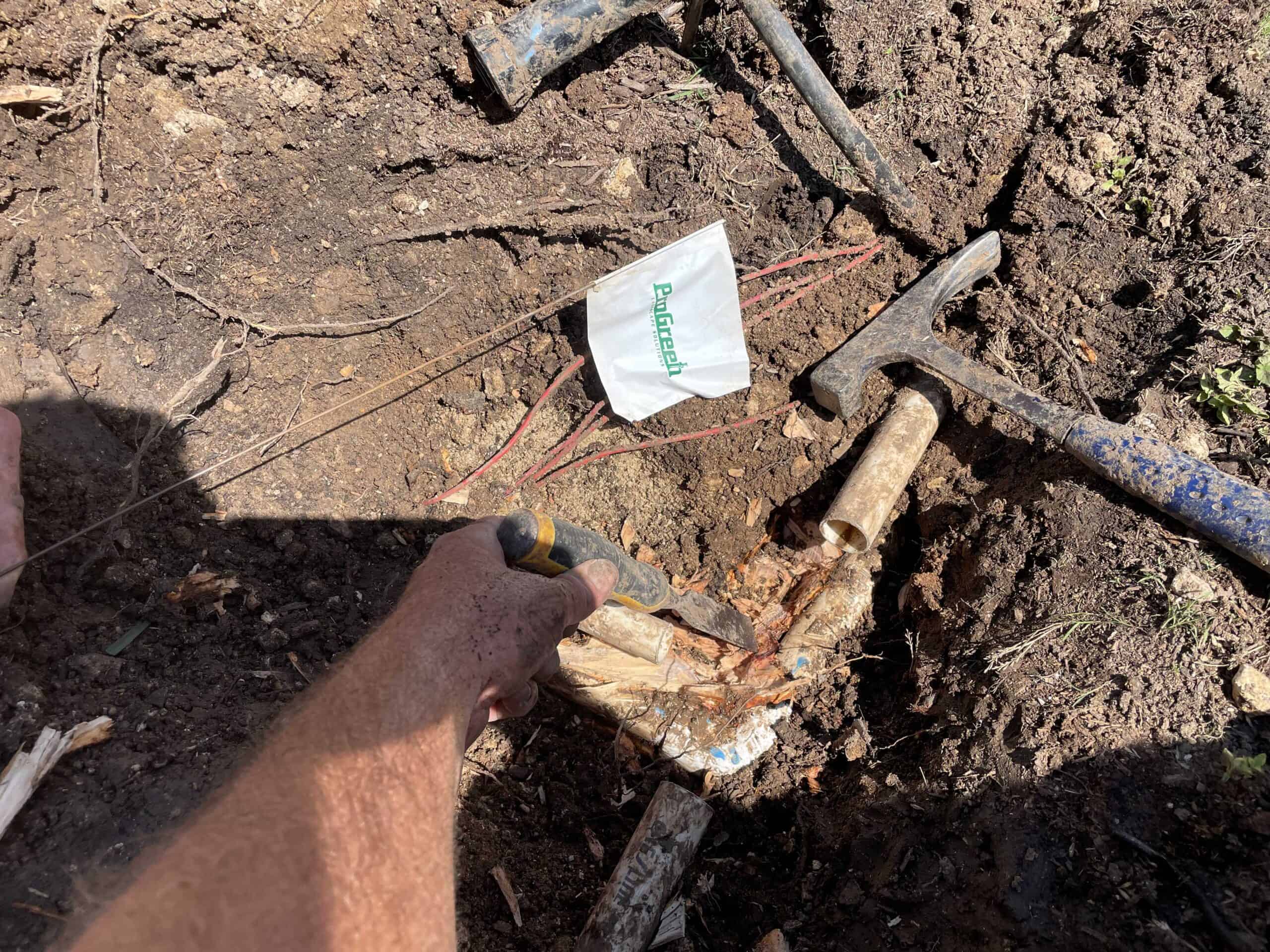 Close-up of irrigation repair process with tools and exposed pipes as technician works on fixing water line leak.