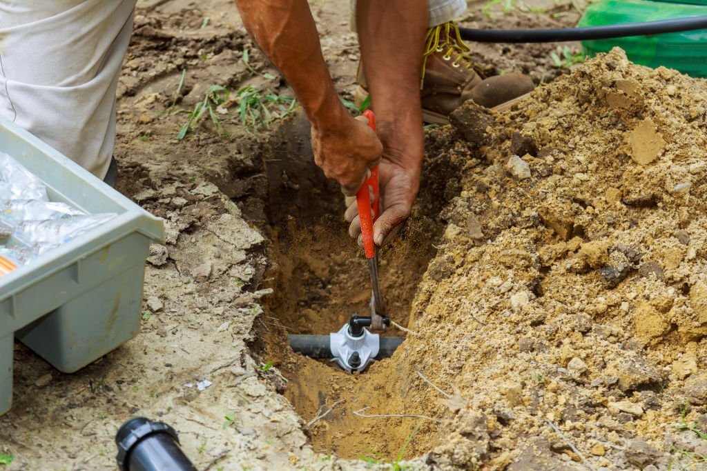 a person repairing their sprinkler by tightening the pipe to prevent leaks.