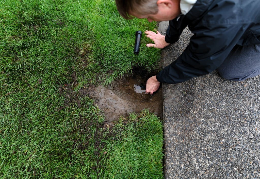 A man shutting off his flooded sprinkler head.