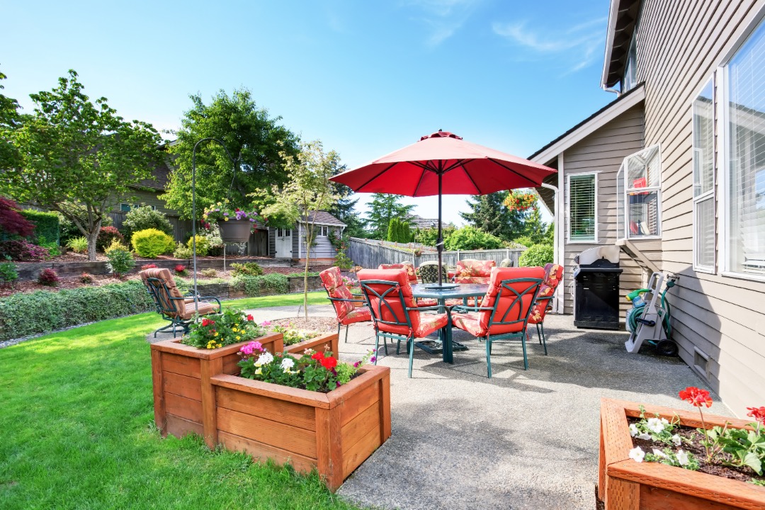 An outdoor living room with wooden planter bed boxes, a red outdoor dining set, and a house.