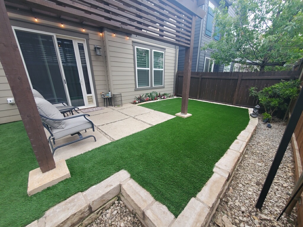 Modern backyard with artificial turf, stone edging, pergola, and concrete patio for low-maintenance outdoor living space.