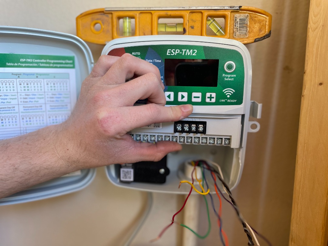 Technician adjusting wires in an ESP-TM2 irrigation controller box during a sprinkler system installation for ProGreen.