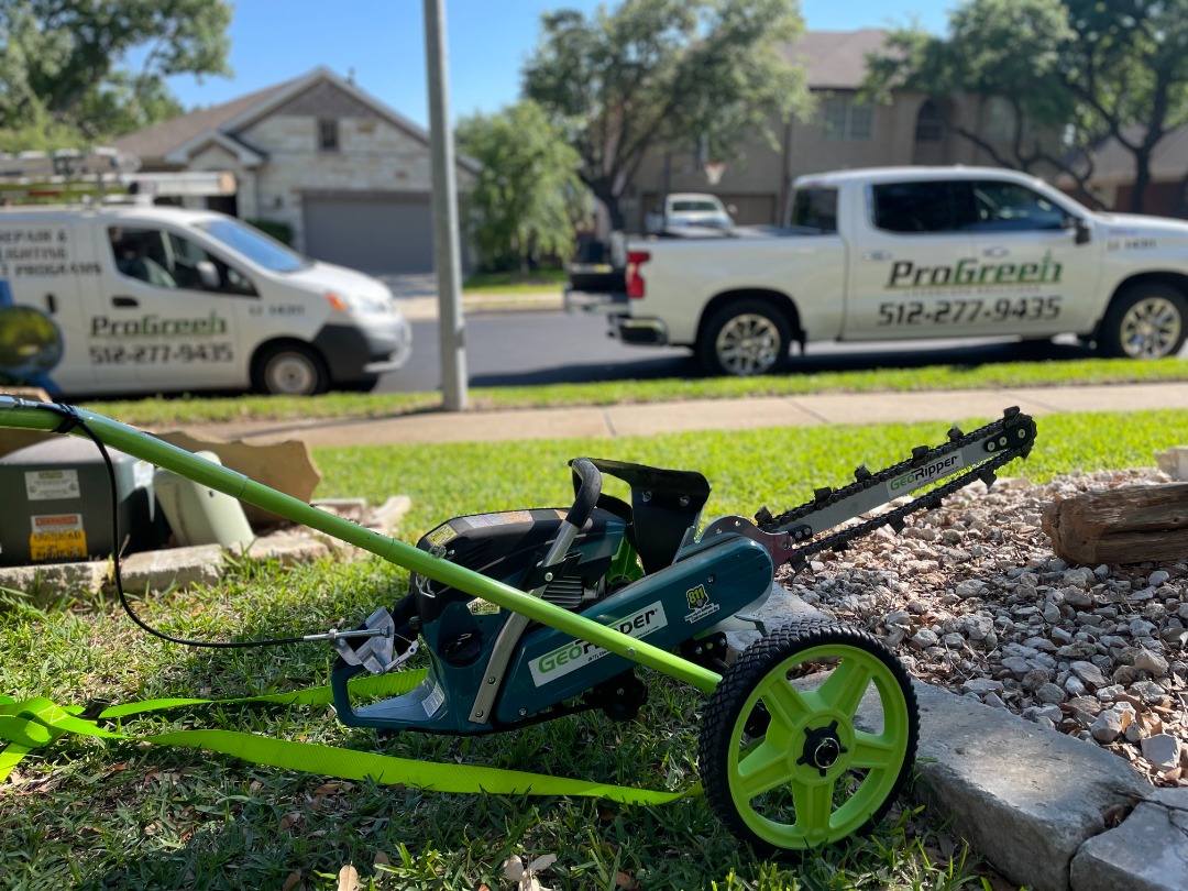 GeoRipper trenching tool on grass with ProGreen service van and truck in background, ideal for irrigation installations.