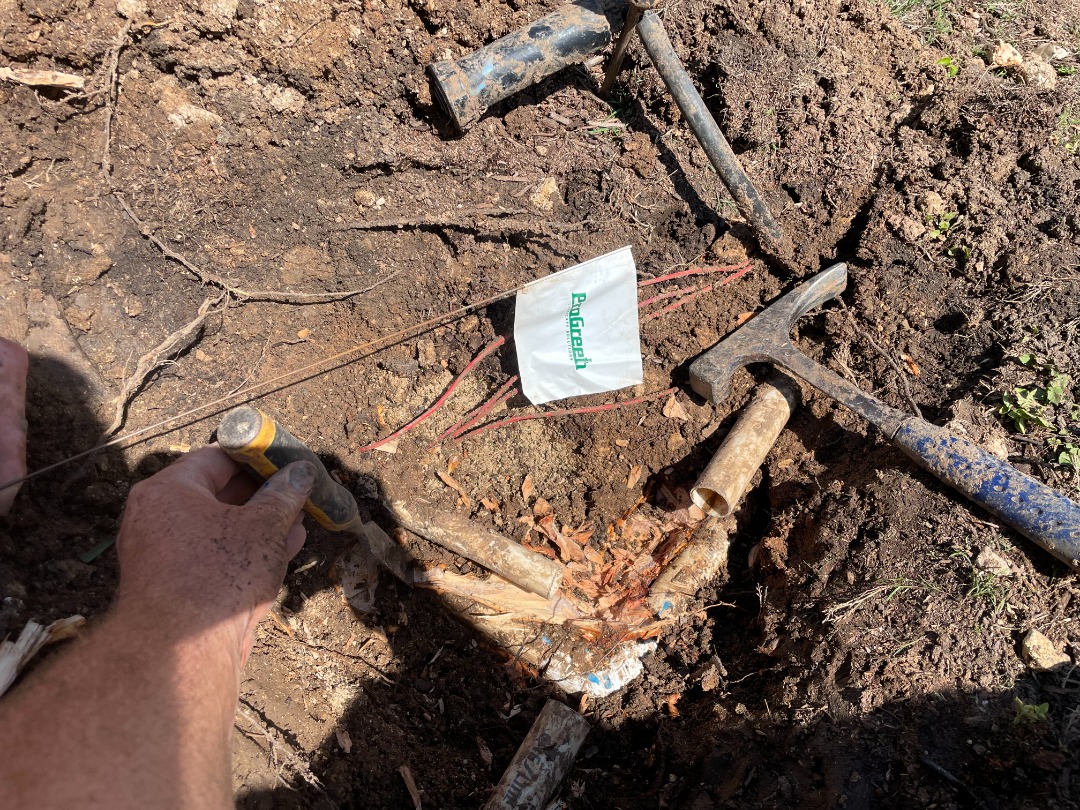 ProGreen technician repairing underground irrigation pipe with tools in dirt and a branded ProGreen utility marking flag.