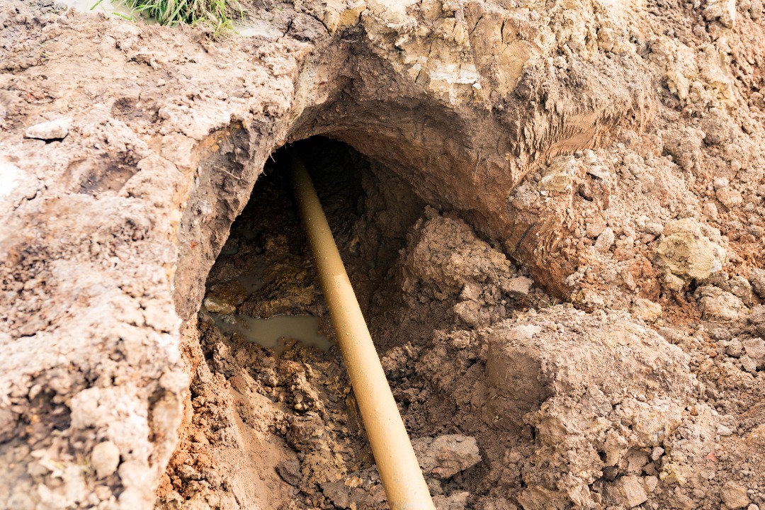 Underground drainage pipe exposed through a freshly dug muddy trench, ready for inspection or connection as part of yard drainage.