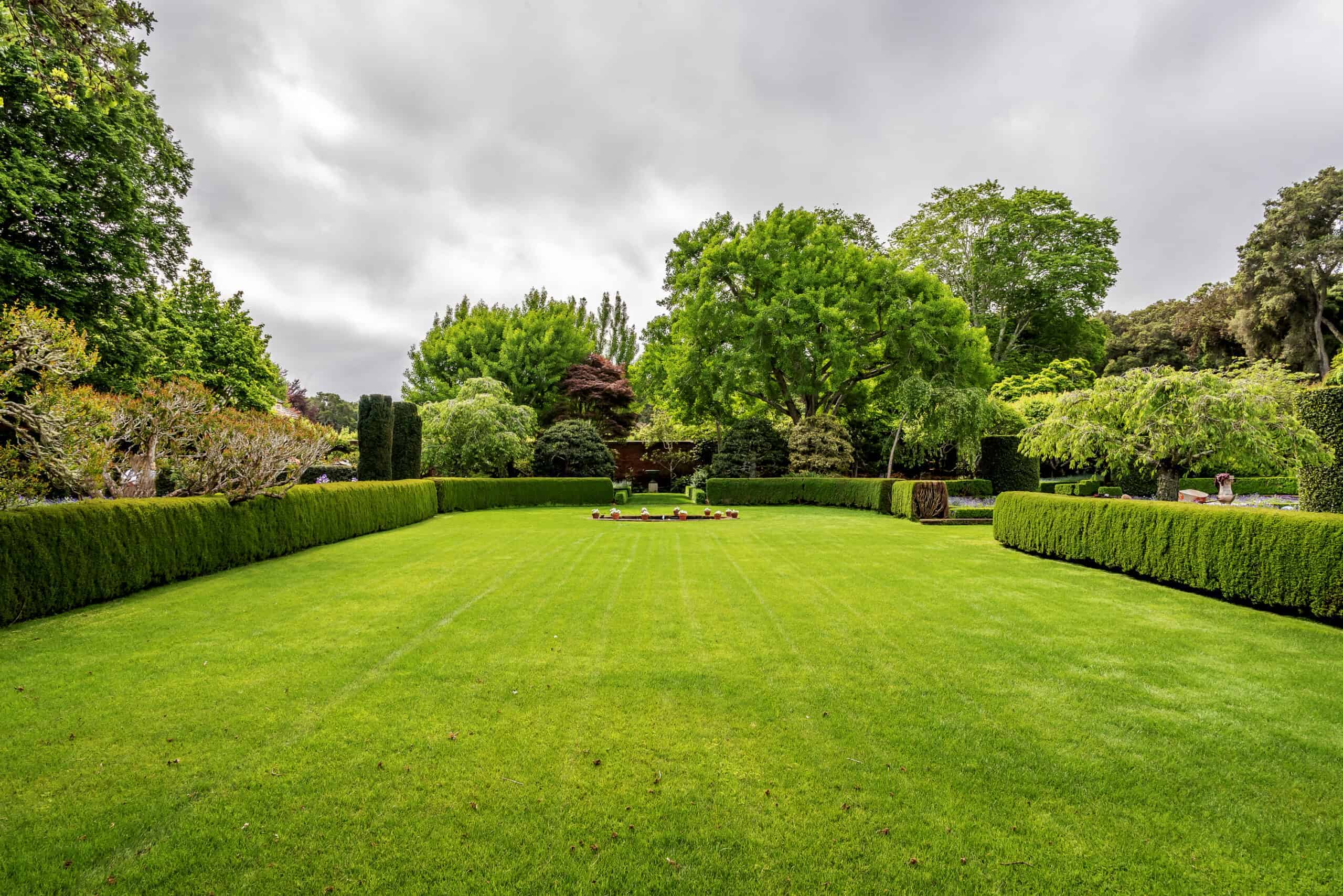 a sprawling green lawn bordered by hedges, mature trees, and custom landscaping