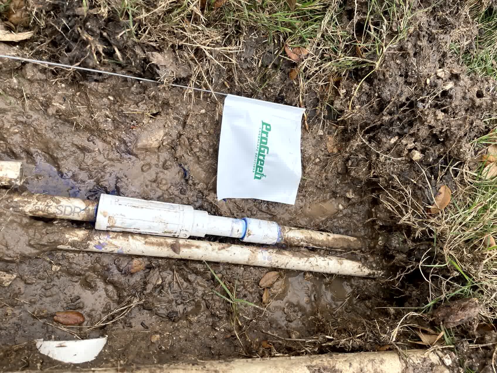 Exposed irrigation pipe prepared for repair in a landscaped yard.