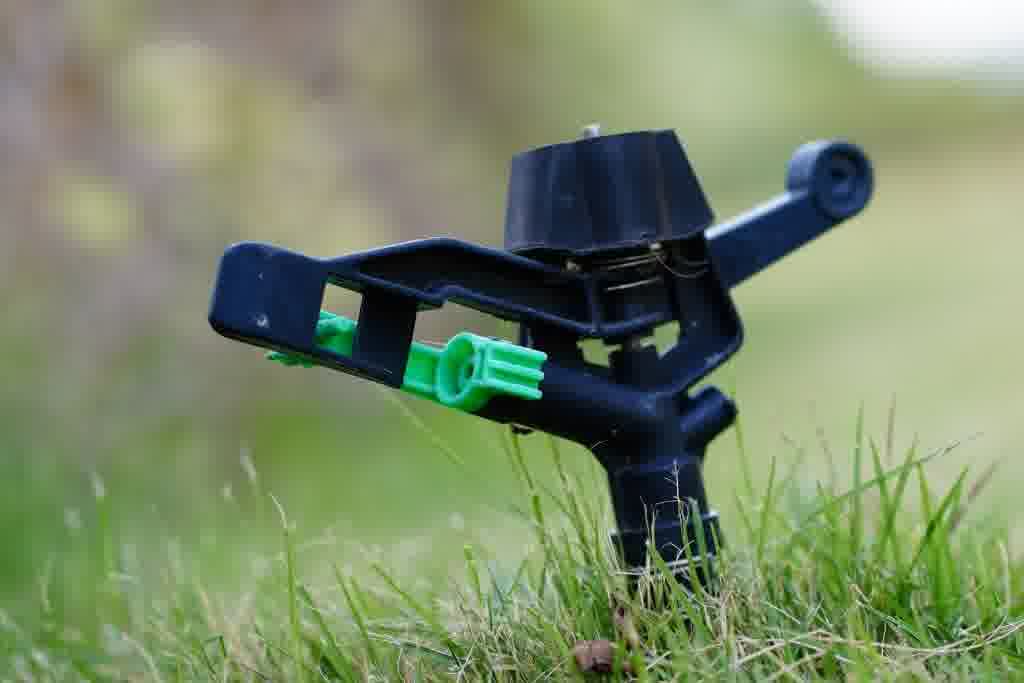 Close-up of a black and green impact sprinkler head on the lawn, part of an irrigation system controlled by an automatic timer.