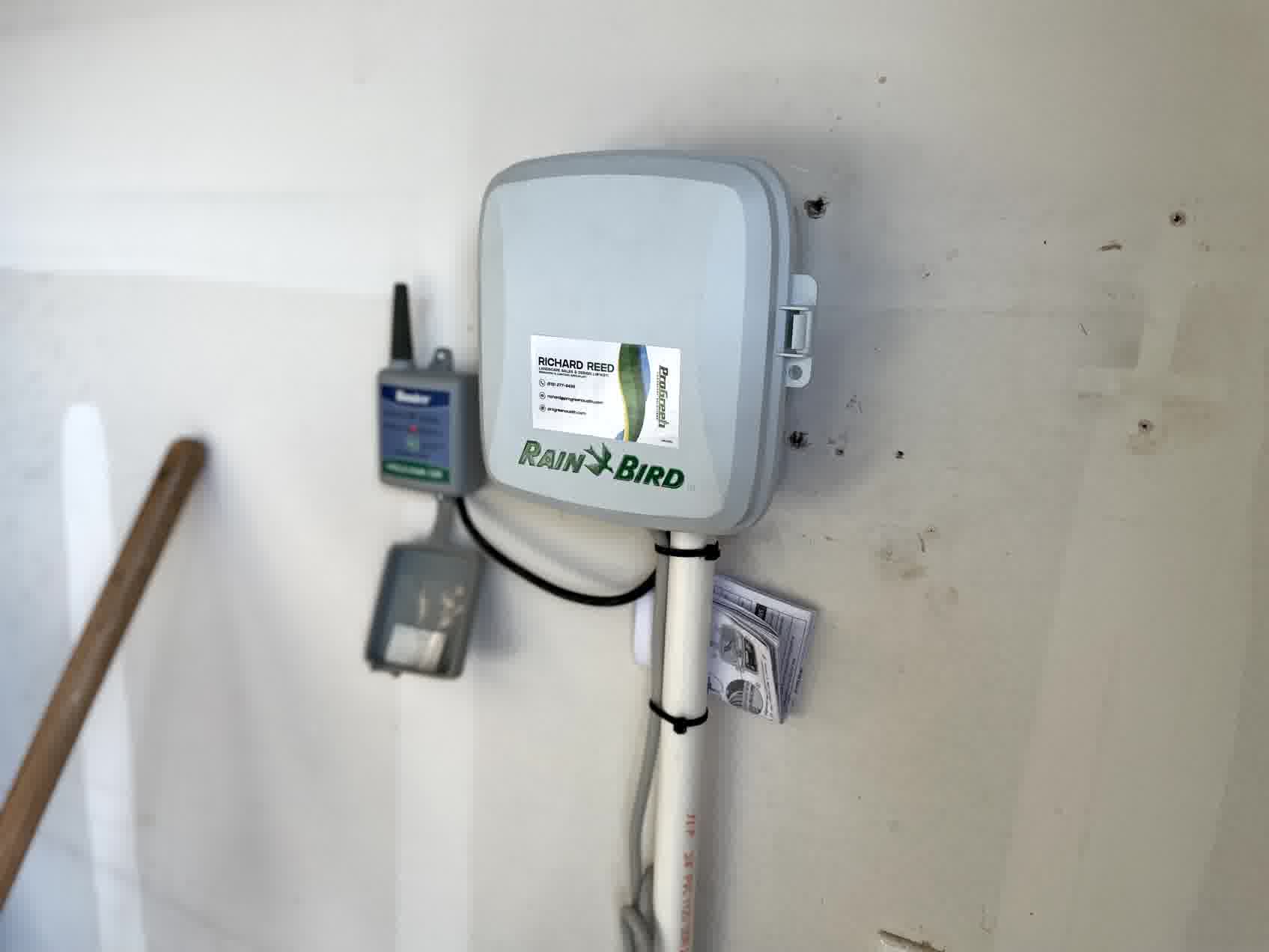 Mounted Rain Bird irrigation controller with wiring and setup guide attached, installed indoors for automated sprinkler system control.