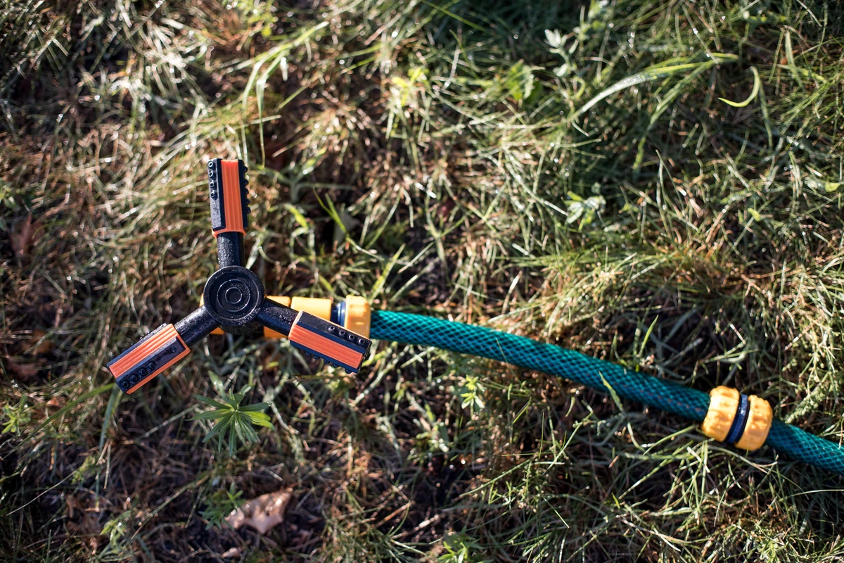 Rotary sprinkler attachment connected to a garden hose on dry grass, not part of a Hunter systems irrigation setup.

