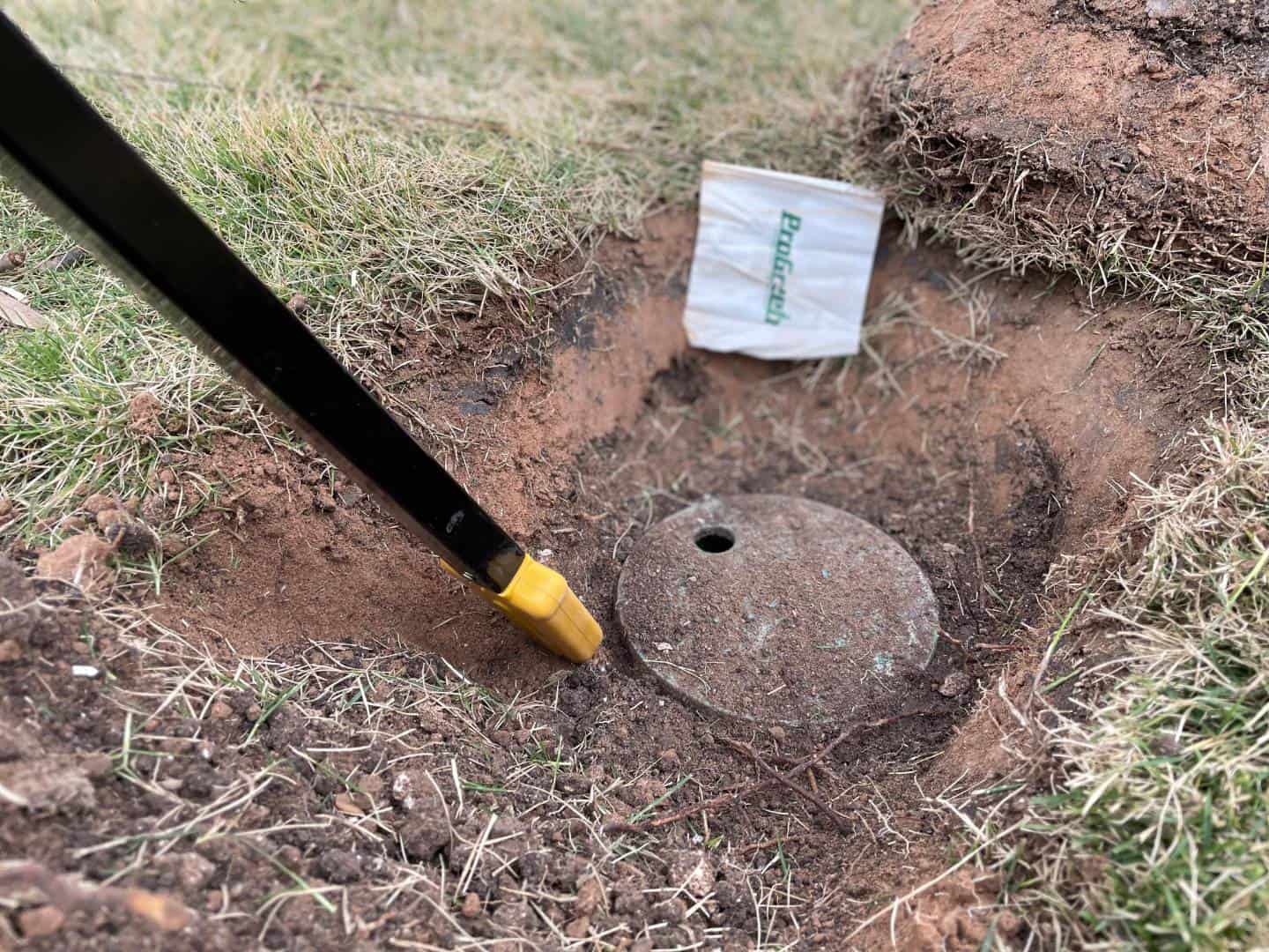 Close-up of an exposed sprinkler valve box being located with an electronic detector for an underground irrigation system inspection.