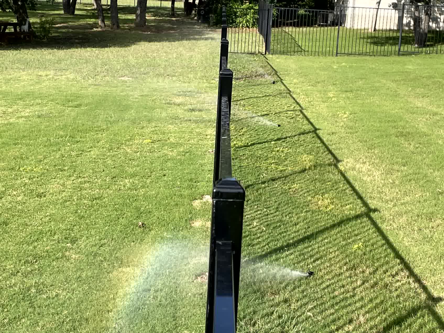 A line of sprinklers next to a black fence.
