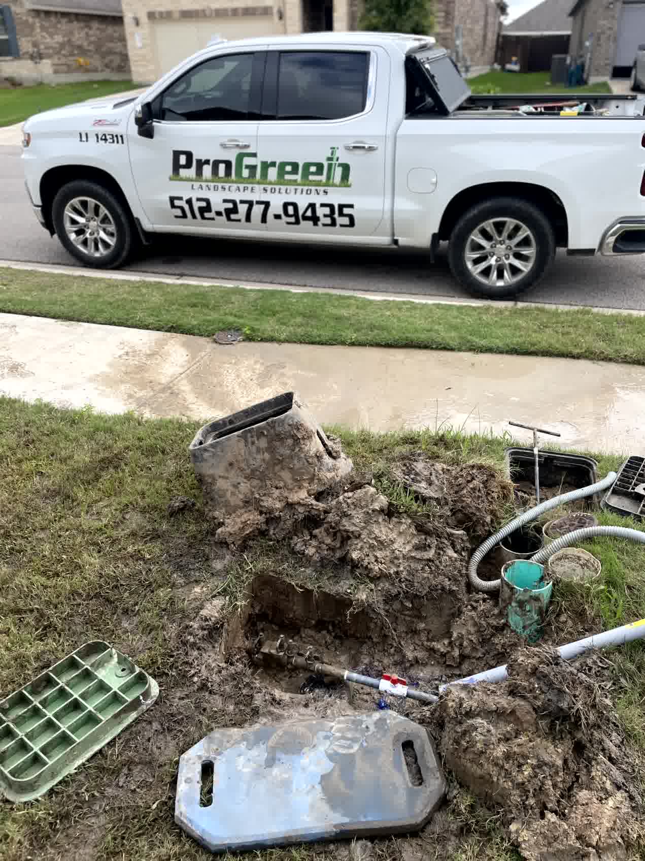Irrigation repair in progress with exposed pipes and muddy soil near a lawn, next to a ProGreen Landscape Solutions service truck.