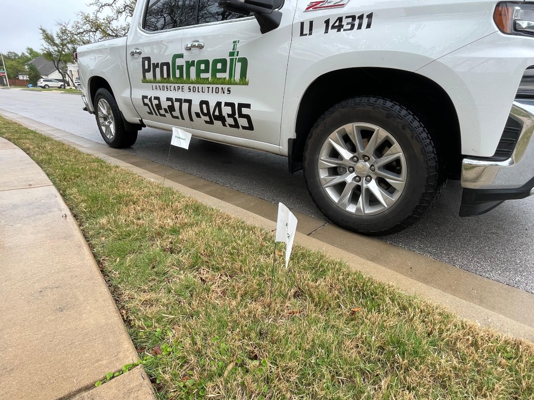 ProGreen service truck parked curbside near irrigation repair flags marking water line locations in residential lawn.
