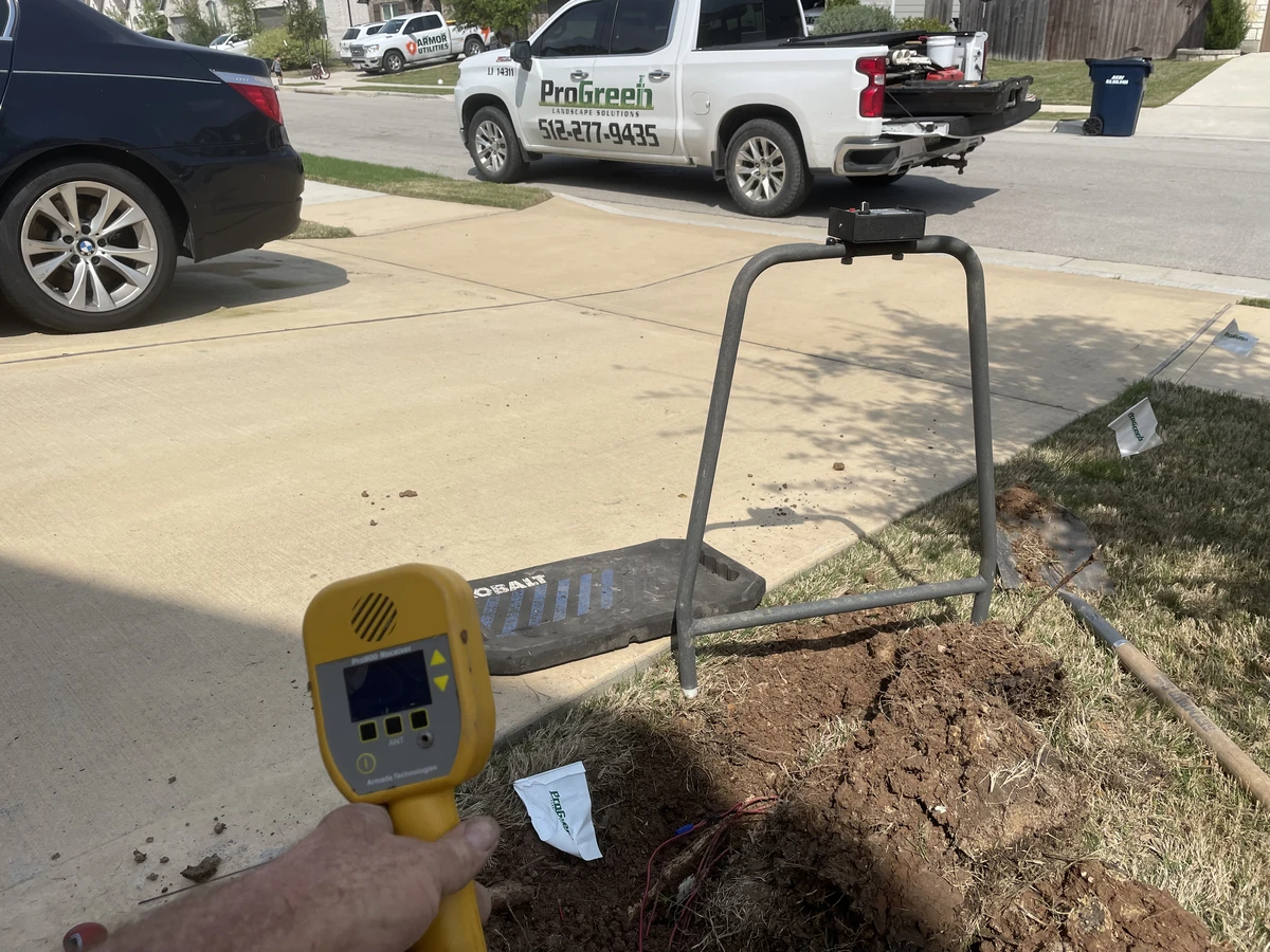 Irrigation inspection technician using electronic wire tracer to locate underground sprinkler valves near residential driveway.
