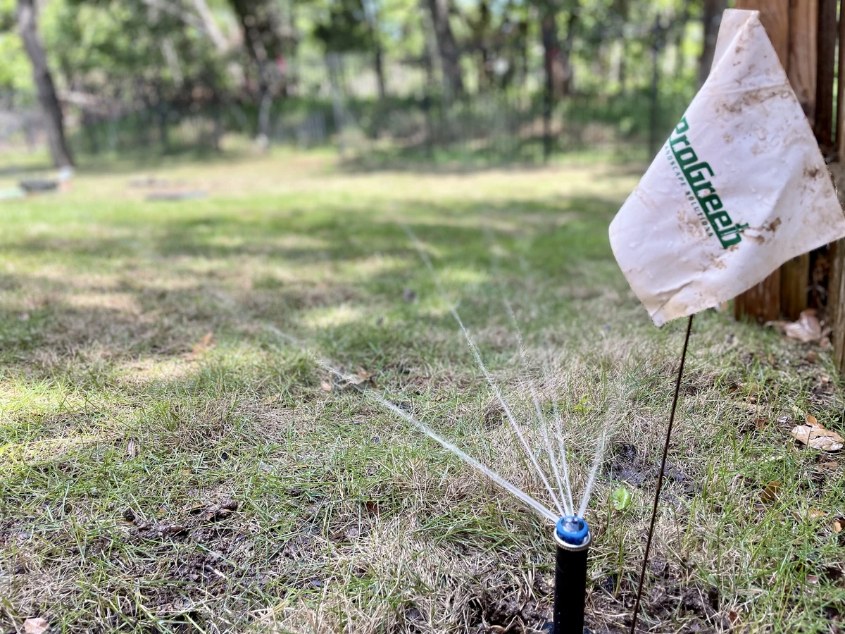 Sprinkler watering patchy grass next to a ProGreen flag, indicating recent sprinkler repair service.
